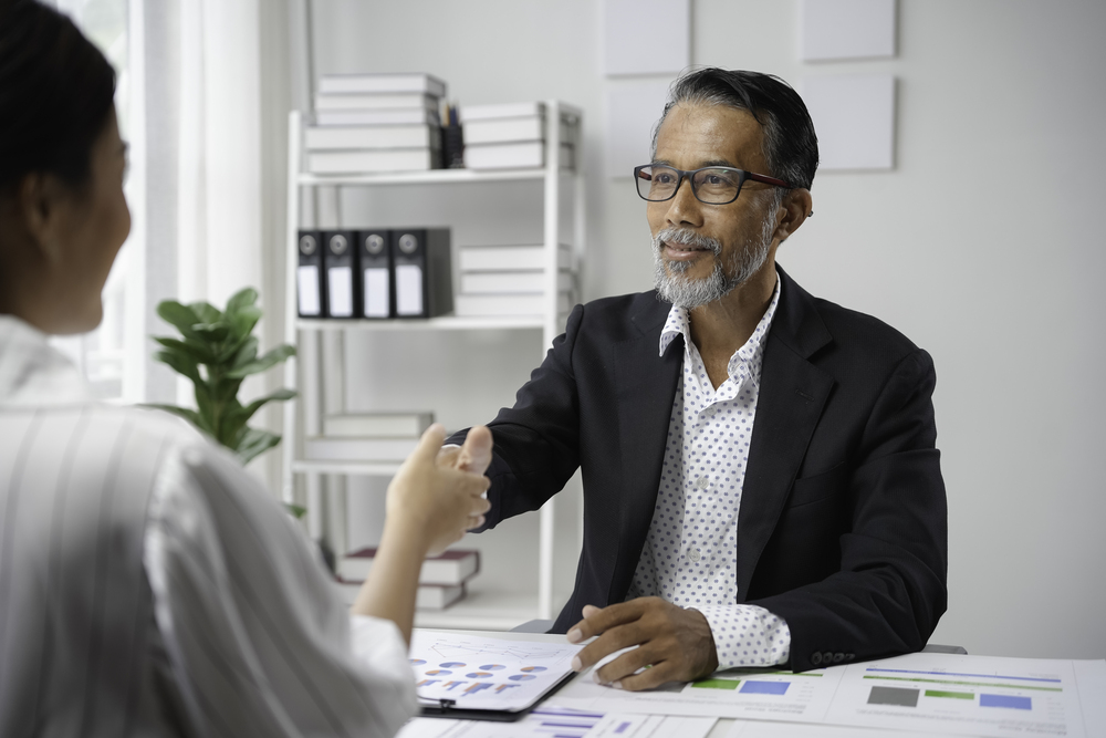 Senior manager shaking hands with a young female professional over a desk in a bright office during a business meeting